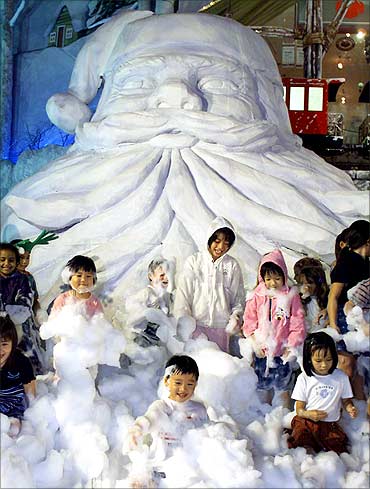 Singaporean children frolic in imitation snow under a giant Santa Claus outside a shopping mall.