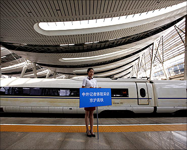A platform guide holds a sign beside a new high-speed train at Beijing South Railway Station.