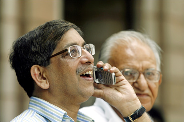 A man speaks on a phone as he looks at a large screen displaying Sensex.