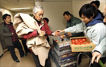 An evacuee receives food from government officers in an aisle at an evacuation centre in Sendai.