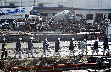 Rescue workers walk in a line to look for survivors at a devastated factory area.