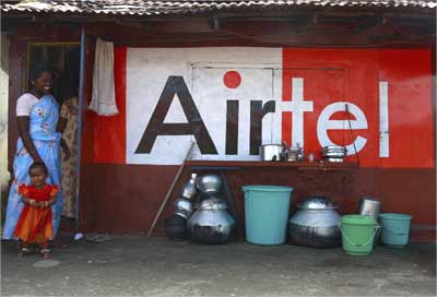 Women and a child stand next to a shop painted with an advertisement of Bharti Airtel in Kochi.