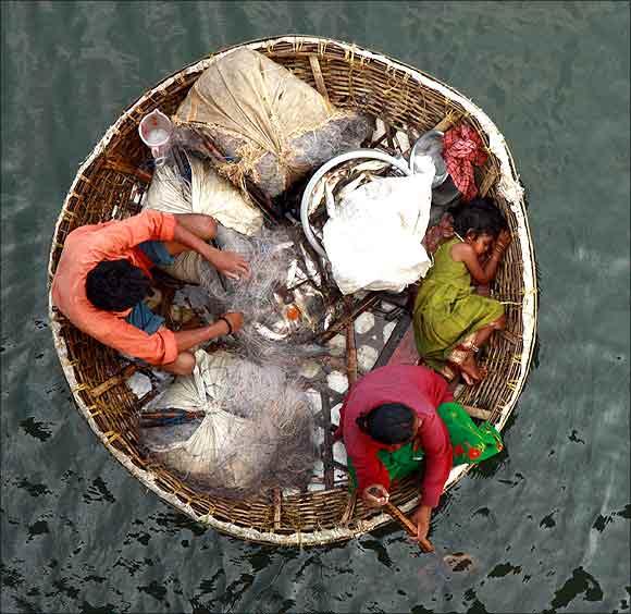 A fisherman arranges a fishing net as his wife paddles their boat in the waters of the Periyar river.