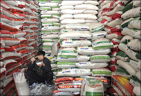 A rice vendor eats a meal among piles of sacked rice at a market in Hefei, Anhui province.