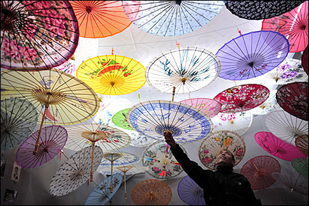 A vendor hangs a Chinese paper umbrella onto a string at his stall in an antique market in Xi'an.