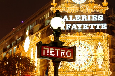 View of a metro sign in front the Galeries Lafayette department store with Christmas lights in Paris.