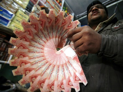 A shopkeeper holds a garland made of Indian currency notes inside his shop at Noida.