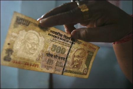 An employee checks a Rs 500 note at a cash counter.