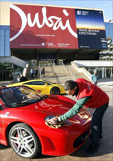 A man cleans a Ferrari car in front of the Cannes Festival Palace with the Dubai tourism logo poster.