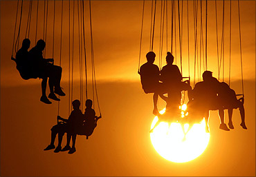 Youngsters enjoy a ride on a circular moving swing in an Athens amusement park at sunset.