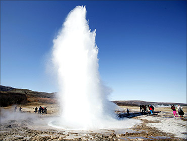 People look at a geyser in Geysir, Iceland.