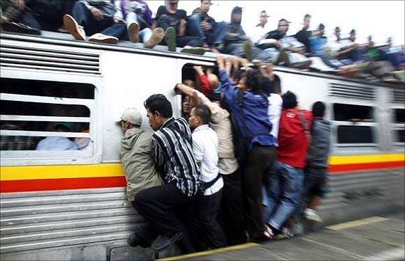 People hang onto an entrance of a commuter train in Depok, Indonesia's West Java province.