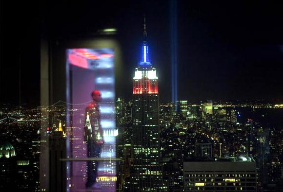A reflection can be seen on a glass barrier in the Top Of The Rock observation deck in front of the Tribute in Light memorial behind the Empire State Building.