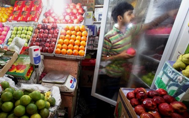 A man takes out an apple from a refrigerator at his fruit stall in Kolkata.