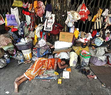 A woman sleeps in front of her belongings, hanging from the shutters of a shop, in Kolkata.