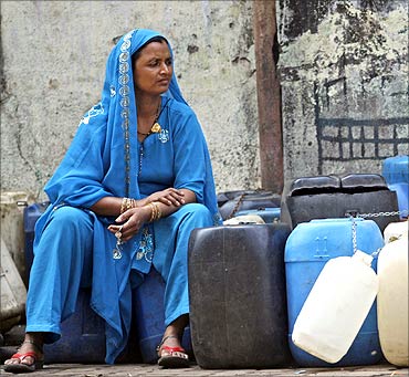 A woman sits on empty water buckets to be filled with drinking water that will be distributed by a water lorry.