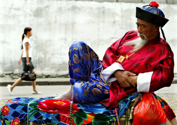 A Chinese man wearing a colourful traditional attire dozes near a tourist shopping district in Shanghai.