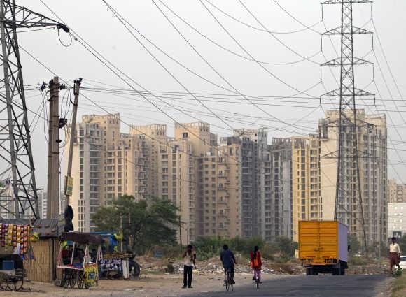 People ride their bicycles under overhead power cables, against the backdrop of multi-storey residential apartments in Gurgaon.