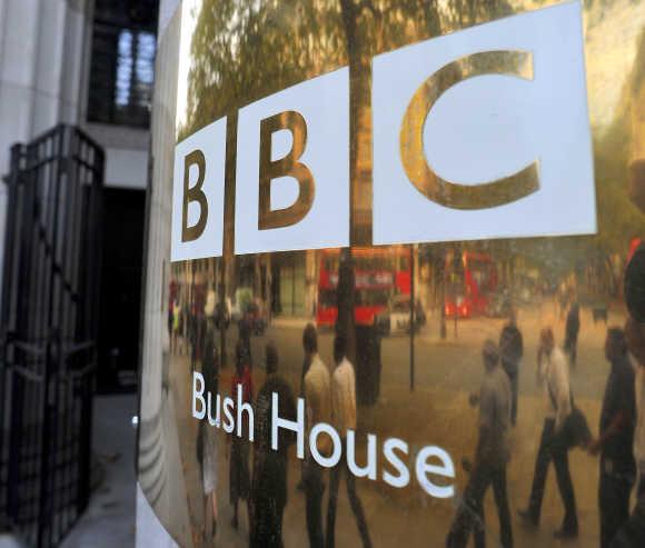 People are reflected in a sign as they walk past British Broadcasting Corporation offices in central London.