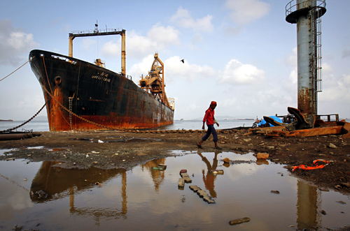 A man walks past a ship docked at a ship breaking yard in Mumbai.
