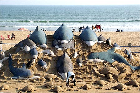 Sand artist Sudarshan Patnaik (C) gives finishing touches to his sand sculpture titled Nature and Environment in Orissa.