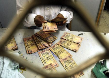 An employee sorts Indian currency notes at a cash counter inside a bank.