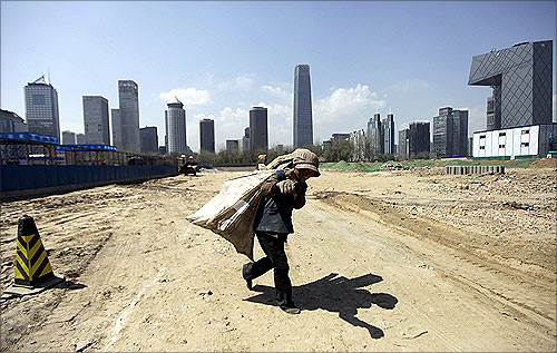 A waste collector carries a sack of recycled material as she leaves a construction site in Beijing's central business district.