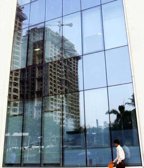 A man walks past a building reflecting the construction of other buildings in Mumbai.