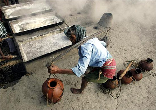 A labourer carries pots of palm juice to prepare jaggery, a form of candy, at a roadside factory in Bagnan, Kolkata.