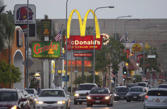 Cars drive past the signs of restaurants along a busy street in Los Angeles.
