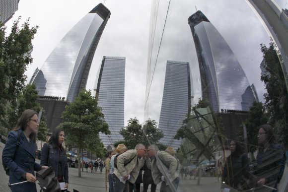 One World Trade Center is reflected inside a window as tourists peer through at the 9/11 Memorial Plaza in New York.