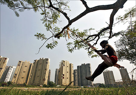 A boy plays on a swing suspended from a tree in front of a residential estate under construction in Kolkata.