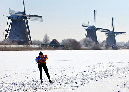 A lone skater skates past three windmills as he enjoys the first time he can skate on natural ice in Kinderdijk, near Rotterdam.