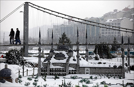 Visitors walk over a model of the Bosphorus bridge with the model of Ottoman-era Sultanahmet mosque in the foregorund at the snow-covered Miniaturk in Istanbul.
