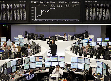Traders are pictured at their desks in front of the DAX board at the Frankfurt stock exchange.