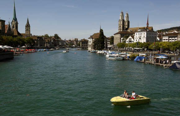 People sit in a boat on the Limmat River during sunny summer weather in Zurich