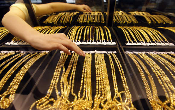 An employee arranges gold jewellery in the counter as her arm is reflected in the mirror at a gold shop in Wuhan, Hubei province, China.
