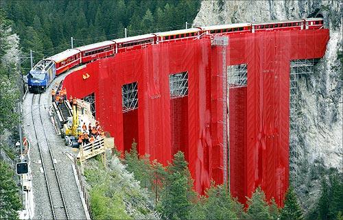 Red cloth veils the scaffoldings at the renovation site of the Landwasserviadukt bridge as a train crosses near the eastern Swiss town of Filisur.