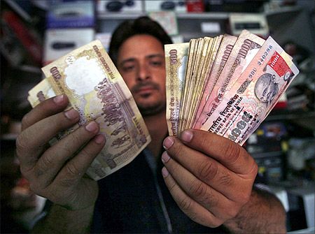 A shopkeeper poses for a picture as he counts Indian currency notes at his shop in Jammu.
