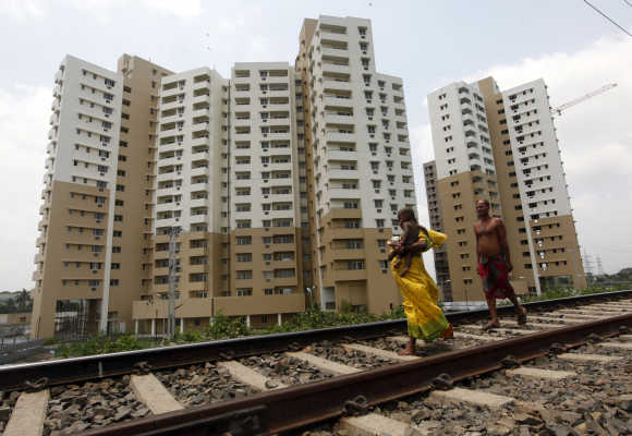 Woman carrying a child walks ahead of her husband on a railway track in front of residential buildings under construction on the outskirts of Kolkata.