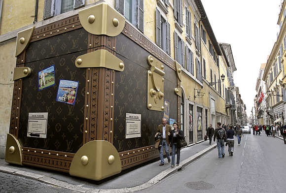 Tourists pass a Louis Vuitton shop closed for refurbishment, its facade covered with a faux suitcase, in Rome.