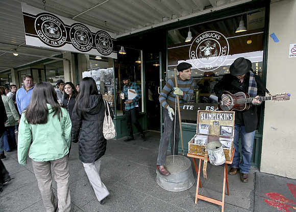 Tourists walk by as street musicians Slimpickins play in front of the first Starbucks store located at historic Pike Place Market in Seattle, Washington.