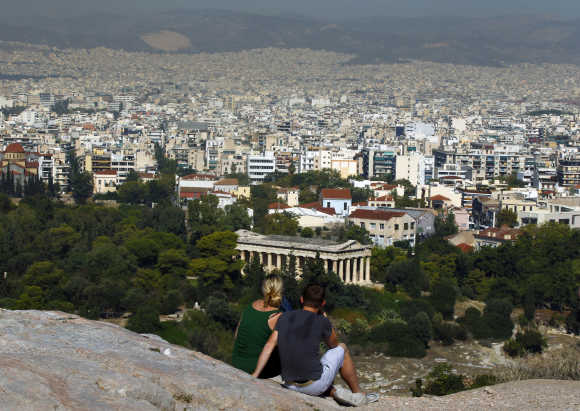 Tourists sit on a hill overlooking Athens outside the archaeological site of the Acropolis.