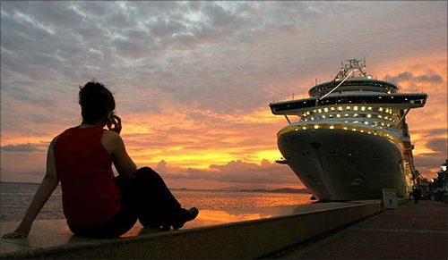 A woman talks on her phone while watching the sun set behind a cruise ship used to house attendees to the Summit of the Americas in Port of Spain, Trinidad.