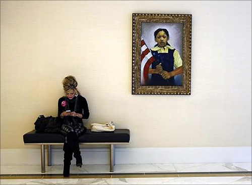 A woman uses her mobile phone as she sits under a portrait of a young girl while attending the Conservative Political Action Conference (CPAC) at National Harbor, Maryland.