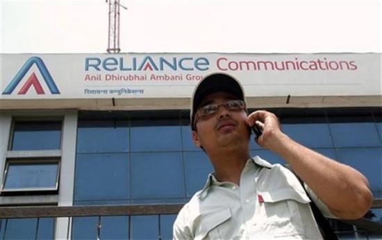 A man talks on a mobile phone in front of an advertisement for Reliance Communications in Mathura.