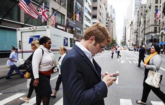 A man uses mobile phone while walking across 5th Avenue in New York.