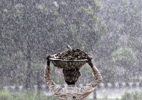 A labourer carries a container of mud as it rains in Noida.