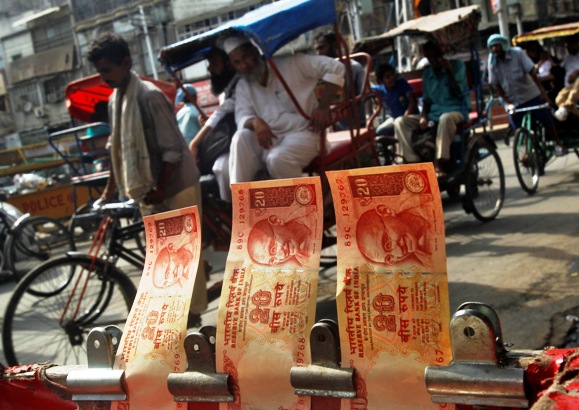 Cycle rickshaws move past a display of Indian rupees at a roadside currency exchange stall in the old quarters of Delhi.