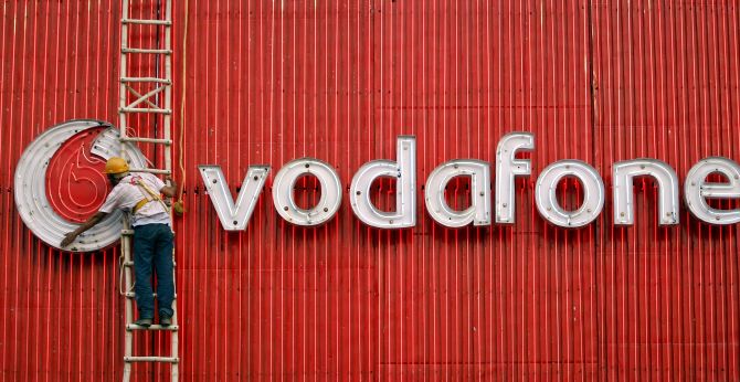 A worker replaces fluorescent lights on a Vodafone billboard in New Delhi.